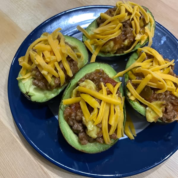 Four avocado halves filled with chili and topped with shredded cheddar cheese on a blue plate.
