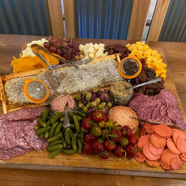 A large charcuterie board with cheeses, meats, honeycomb, olives, pickles, and peppers.
