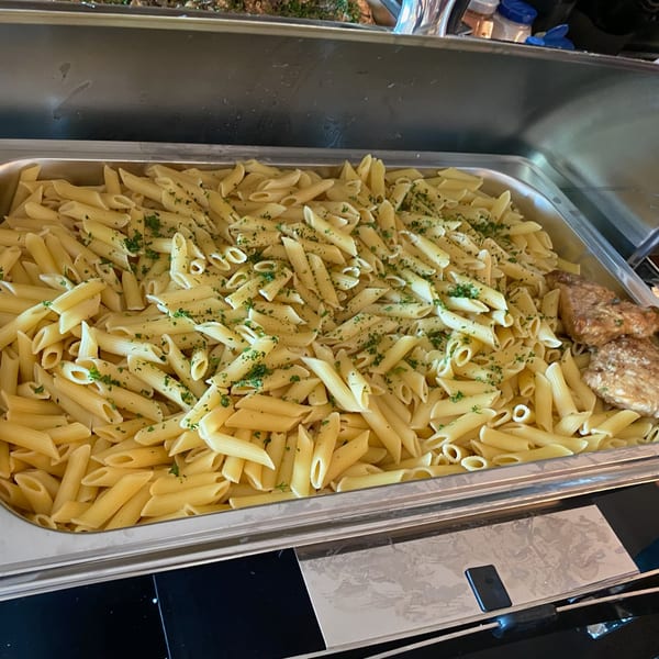 A large metal tray filled with penne pasta and grilled chicken, garnished with parsley.