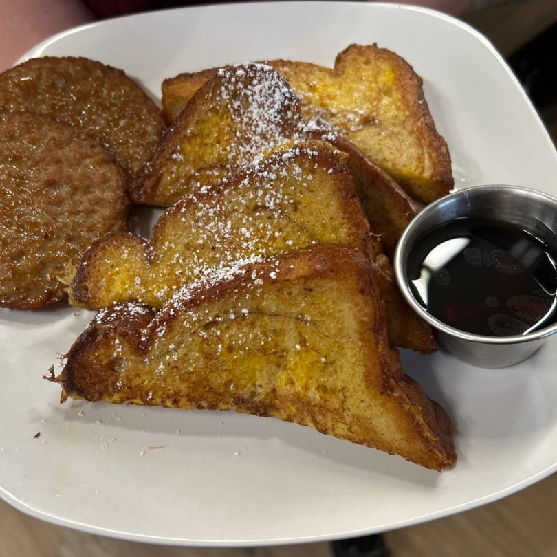 French toast with powdered sugar and a side of syrup on a white plate.