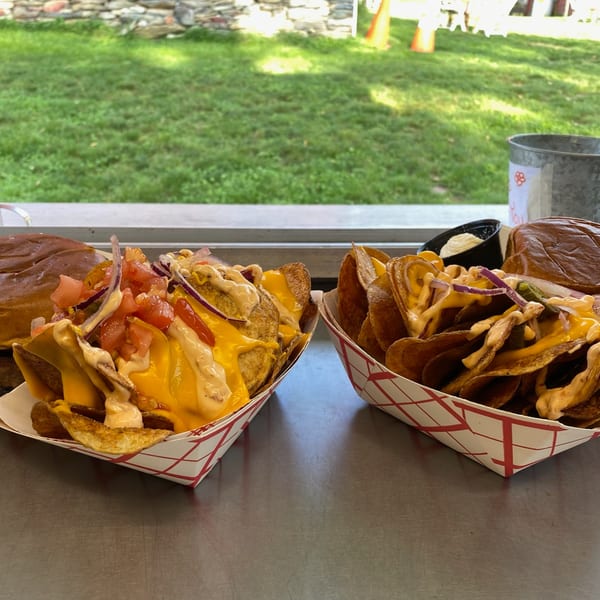 Two baskets of Rustic Tables' loaded potato chips with cheese, tomatoes, onions, and sauce.