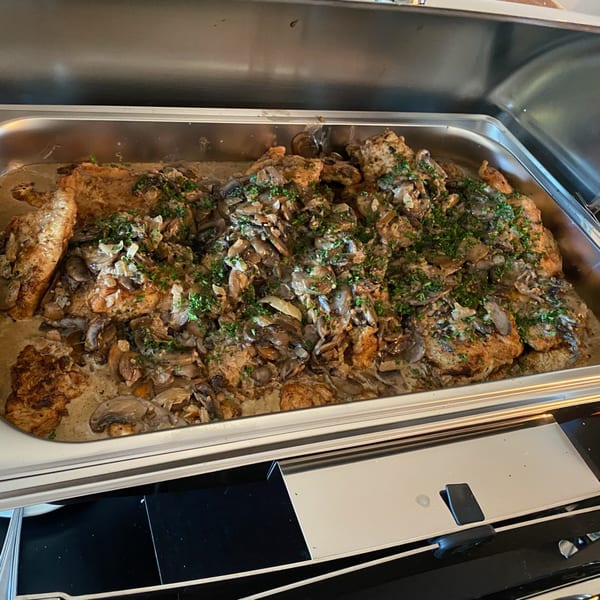 A stainless steel chafing dish filled with chicken and mushrooms in a creamy sauce, garnished with parsley.