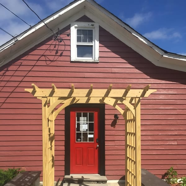 Rustic Tables Restaurant & Bar's red building with a white window and a red door under a wooden archway.