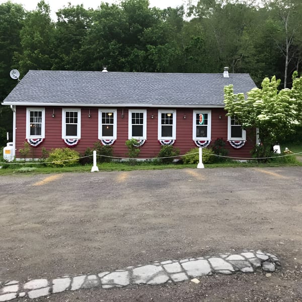 The Rustic Tables Restaurant & Bar, a red building with white trim, sits behind a gravel parking lot.