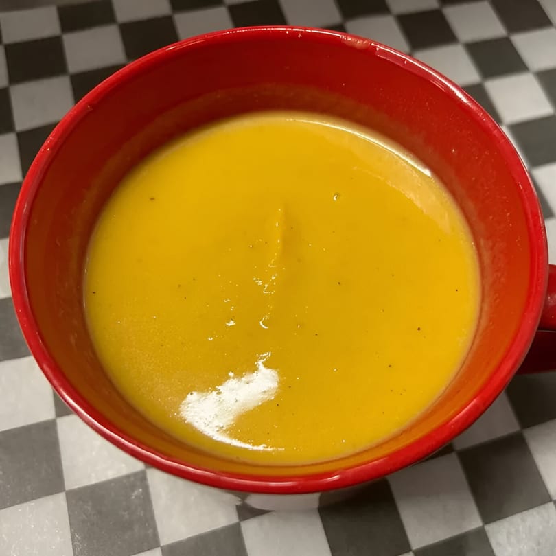 A vibrant orange soup in a red bowl sits on a black and white checkered surface.